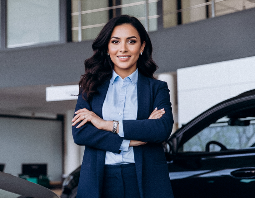 Mujer profesional con traje y brazos cruzados, sonriendo en el interior de una agencia de autos.